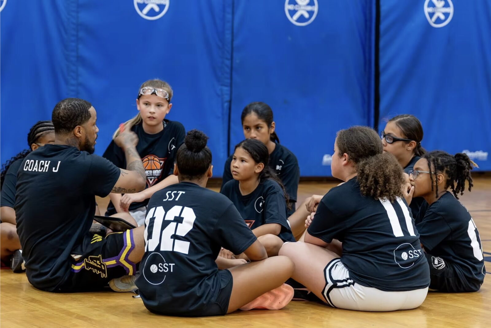 A coach speaking with a team of young players on the sideline.