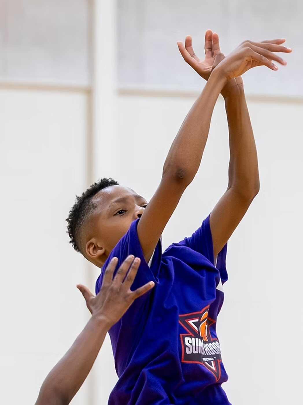 A young player follows through on a jump shot, arms extended overhead.